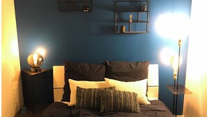 A bedroom with a bed, two bedside tables, a wall-mounted shelf, and two floor lamps.