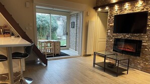 A modern living room with a stone fireplace, a dining area with a table and chairs, and a staircase leading to a balcony.