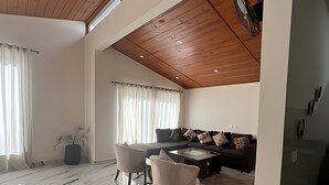 A spacious living area with a high ceiling, wooden beams, a marble floor, a sofa set, and a dining table. - Alpine Crest Cottages (Abbottabad)