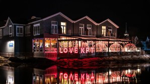 Un edificio con un letrero iluminado grande que dice "LOVE KPT" y su reflejo en el agua.