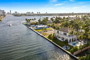 A waterfront property with a pool, palm trees, and a view of the city skyline.