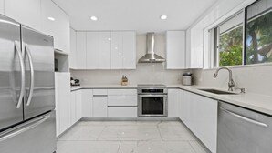 A modern kitchen with stainless steel appliances, white cabinetry, a built-in oven, and a window with a view of greenery.