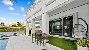 A modern outdoor patio with a pool, a dining area with metal chairs, and a hanging chair.