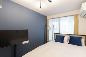 A hotel room with a bed, a flat-screen TV, a window with curtains, and an air conditioning unit. - Repure Higashimukojima Ekimae Residence II (Tokyo)