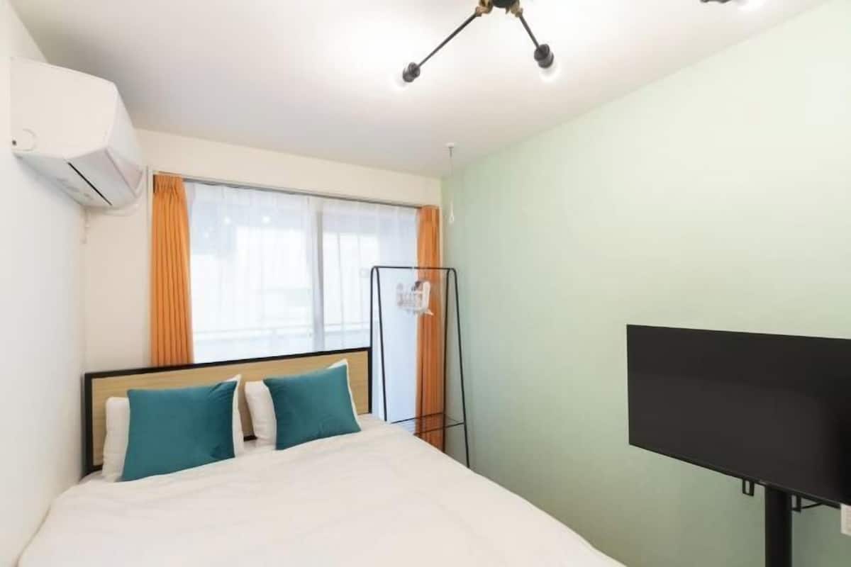 A hotel room with a bed, a TV, an air conditioning unit, and a window with curtains.