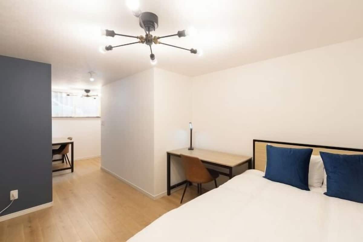 A bedroom with a bed, a desk, and a chair. There is a ceiling light fixture above the bed.