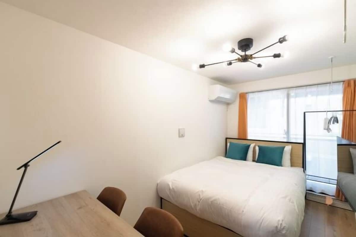 A hotel room with a bed, a desk, a chair, a lamp, and a ceiling light fixture.