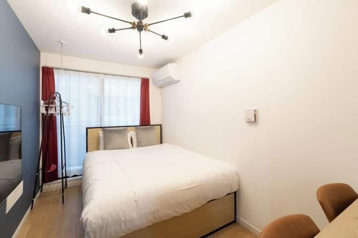 A bedroom with a bed, a desk, a chair, a TV, and a ceiling light fixture.