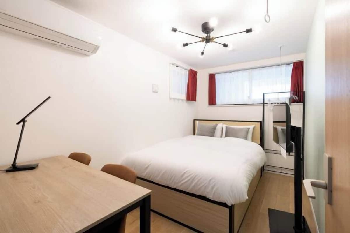 A hotel room with a bed, a desk with a chair, a desk lamp, a TV, and a window with curtains.