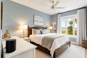 Une chambre à coucher comprenant un lit, des lampes de chevet, une table de chevet, un ventilateur de plafond, une fenêtre avec des rideaux et une vue sur l’extérieur.