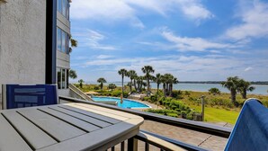 A balcony with a pool, palm trees, and a view of the water. - 1906 South Beach Club - Just a Few Steps from Pool Days and Beach Waves! (Hilton Head Island)