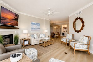 Un salon comprenant un canapé, une table basse et des fauteuils, une cheminée, et un coin repas à l’arrière-plan.
