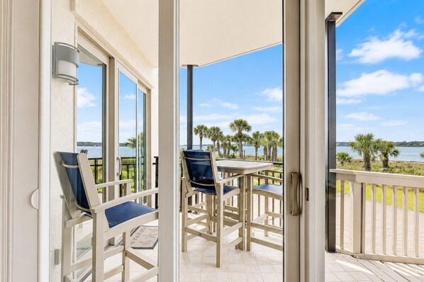 Un balcon avec une table et des chaises, une vue sur la plage et des palmiers.