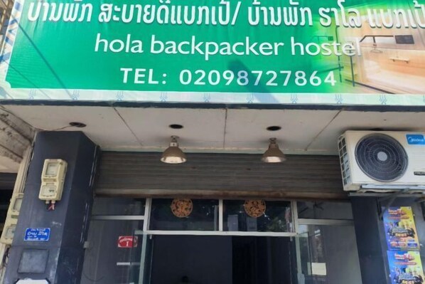 Un hostal con un letrero verde que anuncia servicios en tailandés y un número de contacto.