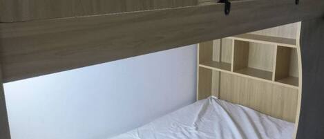 A bunk bed with a wooden headboard and a lower bunk with a white mattress.