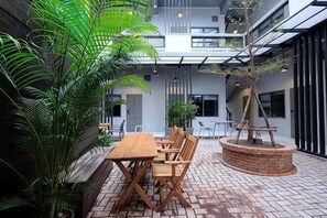 A courtyard with a wooden table and chairs, surrounded by potted plants and a brick planter with a tree. - Sailomyen Cafe and Hostel (Vientiane)