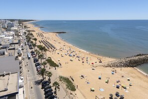 A beach with rows of umbrellas and sun loungers, a rocky breakwater, and a clear blue sky.