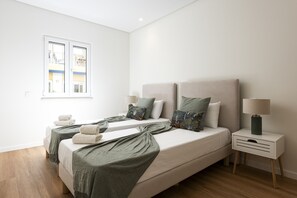 A modern hotel room with two beds, a window, a bedside table with a lamp, and a wooden floor.