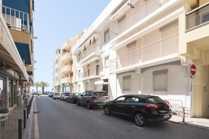A street lined with multi-story buildings, parked cars, and a clear sky.