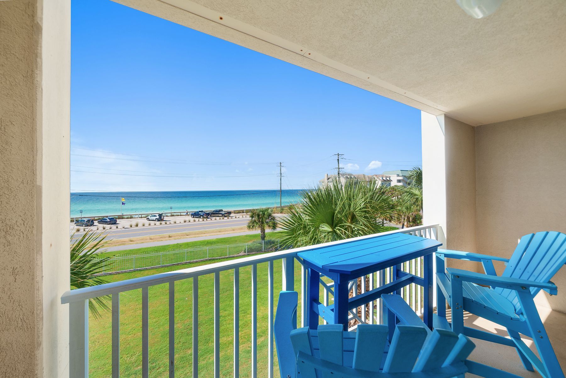 A balcony with a view of the beach, a table, and two chairs.