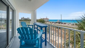 A balcony with blue chairs and a table, overlooking a beach with buildings and a clear sky. - Premier Gulf Views • Private Balcony • Freshly Updated | Amalfi 303A (Miramar Beach)