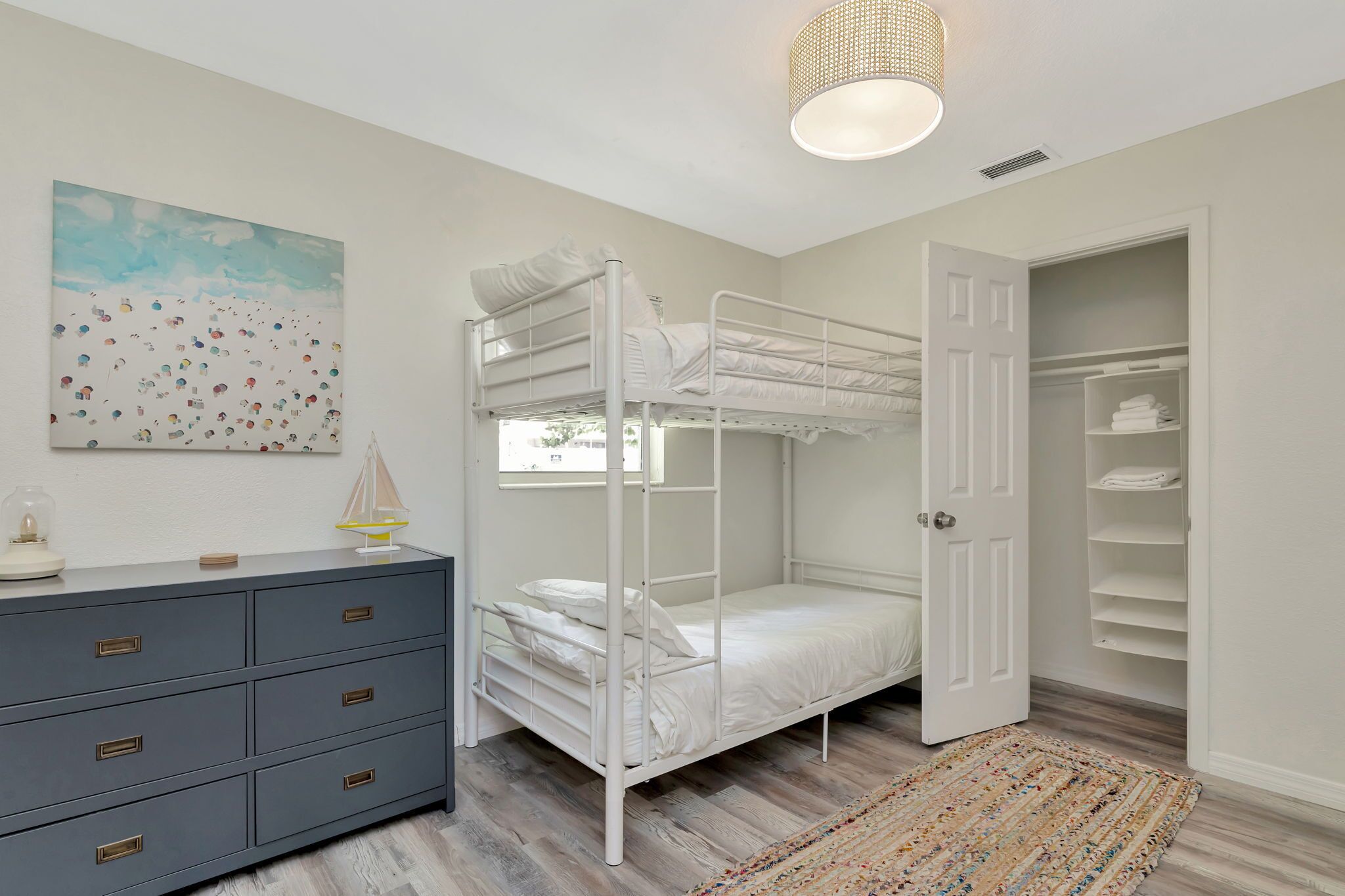 A bunk bed room with a dresser, a painting, and a closet.