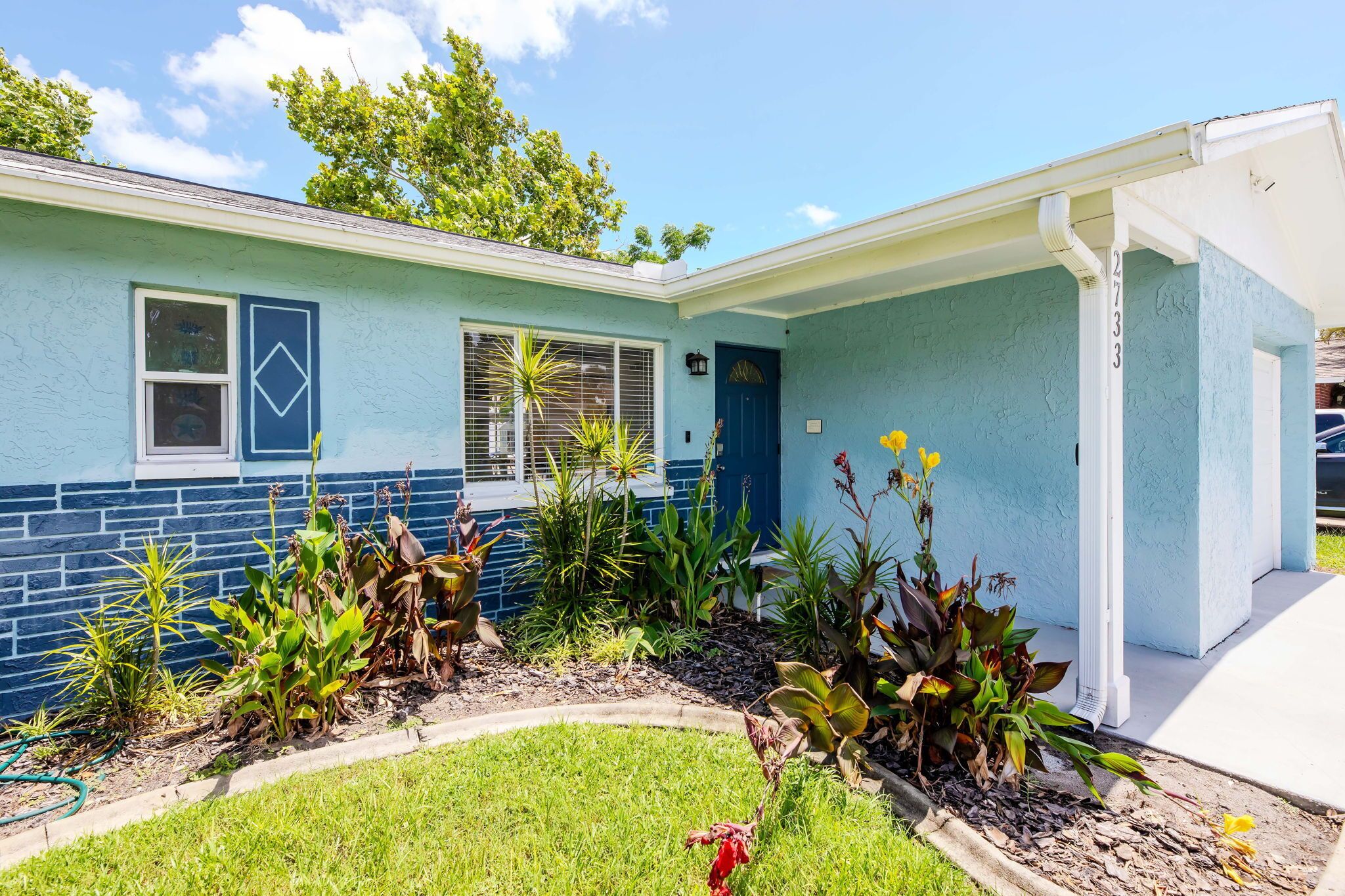 A house with a blue exterior, a front porch, and a garden with various plants.