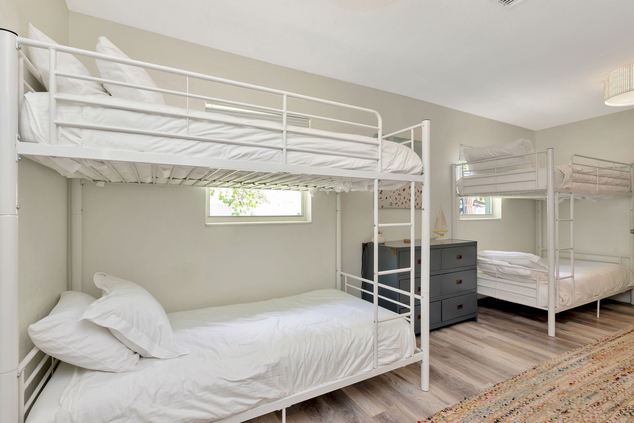 A bunk bed room with a dresser and a window.