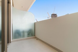 Un balcon doté d’une paroi en verre, d’un sol carrelé et offrant une vue sur un chantier de construction en arrière-plan.