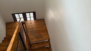 A wooden staircase with a handrail, leading to a landing with a window. - BLISS STAYS (Kanayannur)
