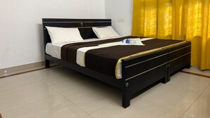 A neatly made bed with a black frame, white and brown bedding, and a water bottle on the bed. - BLISS STAYS (Kanayannur)