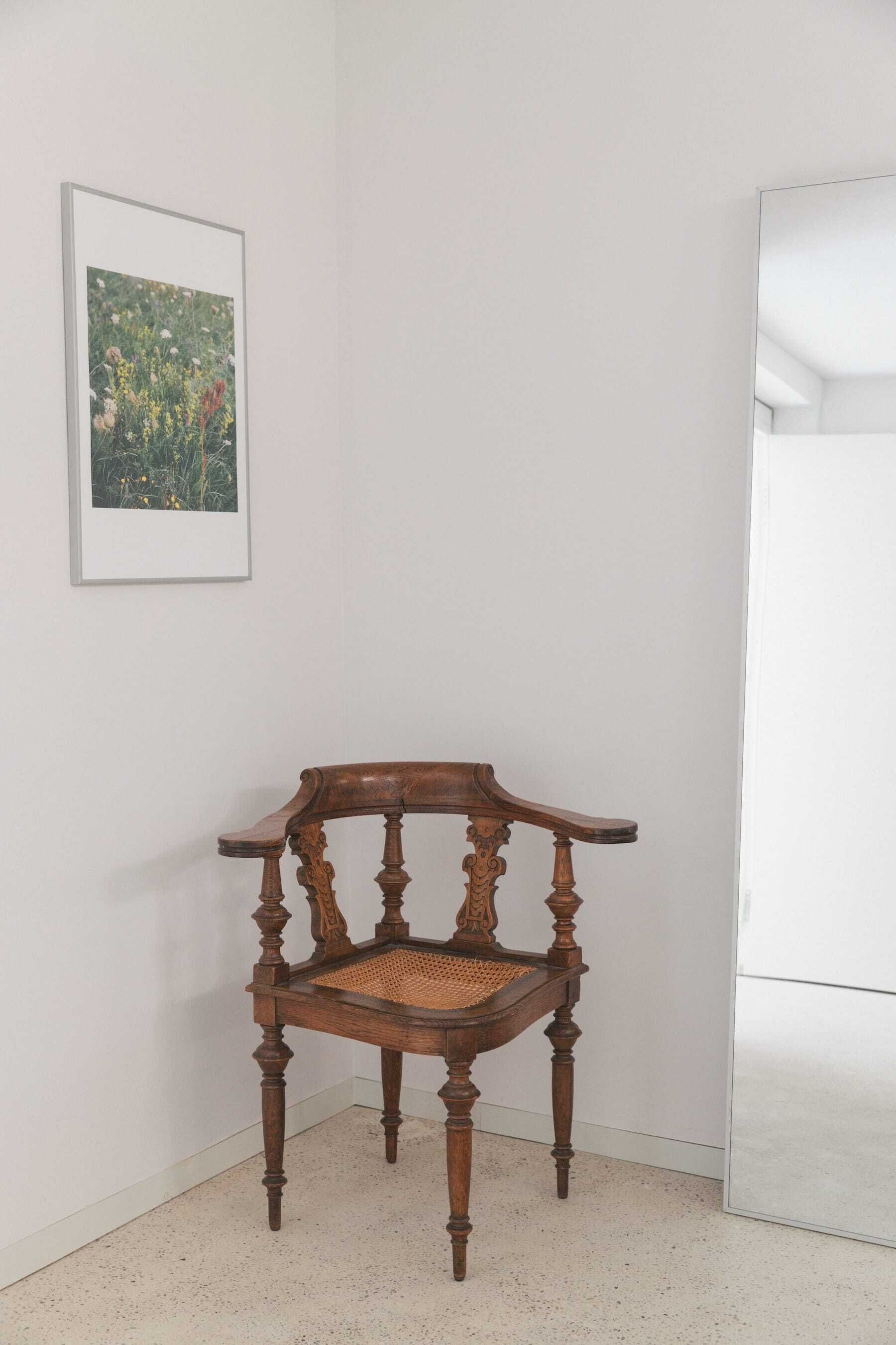 A corner of a room with a wooden chair and a framed picture on the wall.