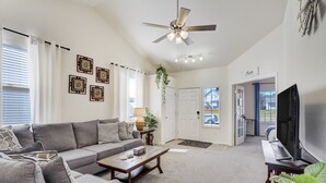 A living room with a gray sofa, a wooden coffee table, a ceiling fan, and a flat-screen TV. - The Cozy Oak | Main Level Comforts (Fountain)