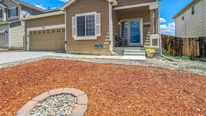 A two-story house with a garage, a covered porch, and a landscaped front yard with mulch and a fire pit. - The Cozy Oak | Main Level Comforts (Fountain)