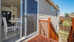 A deck with a wooden railing, a sliding glass door leading to a dining area with white chairs and a table, and a view of a backyard with a wooden fence. - The Cozy Oak | Main Level Comforts (Fountain)
