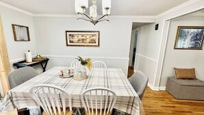 A dining room with a table covered in a plaid tablecloth, white chairs, a chandelier, and framed artwork on the walls. - Spacious 5-bedroom house in lovely Amherst with Central AC, (Buffalo)