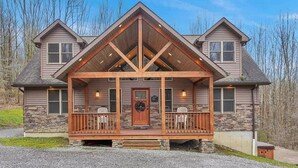 Eine zweistöckige Blockhütte mit Stein Fundament, einer hölzernen Veranda mit zwei Stühlen und einer mittleren Tür mit einem Kranz.
