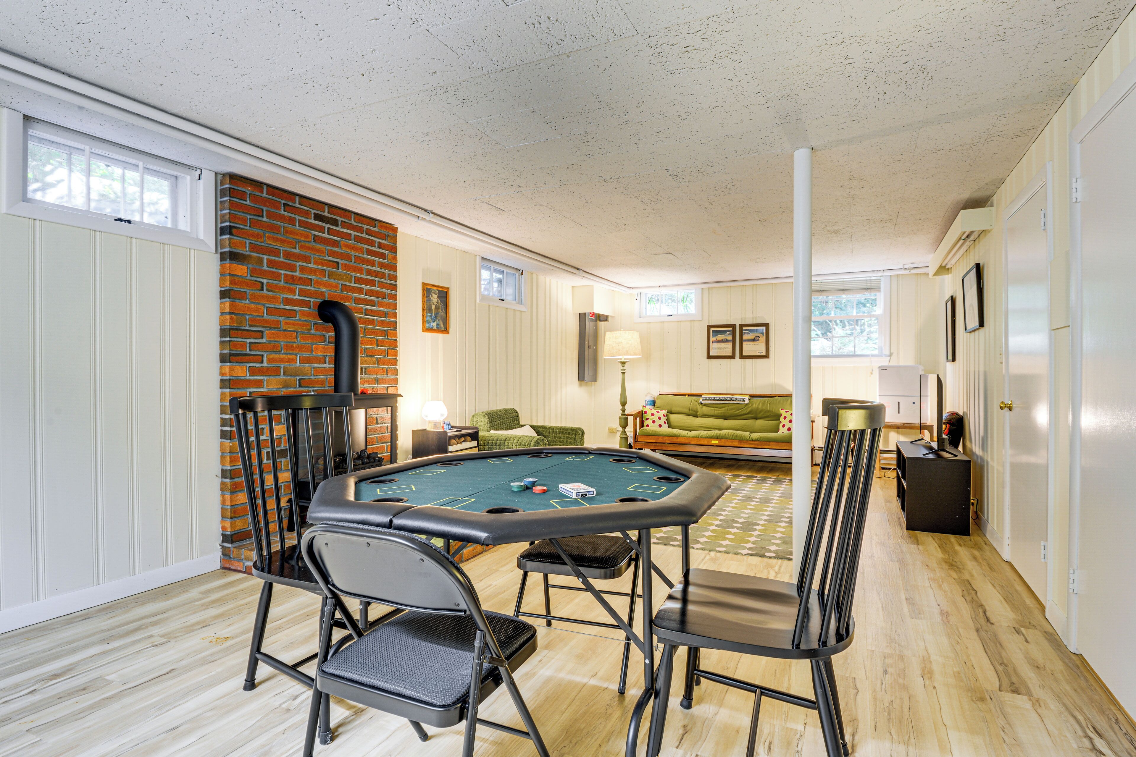 A room with a pool table, chairs, a green sofa, and a brick wall.