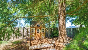 Une structure rustique en bois, dotée d’un toit en pente, entourée d’un feuillage dense et d’un grand tronc d’arbre.