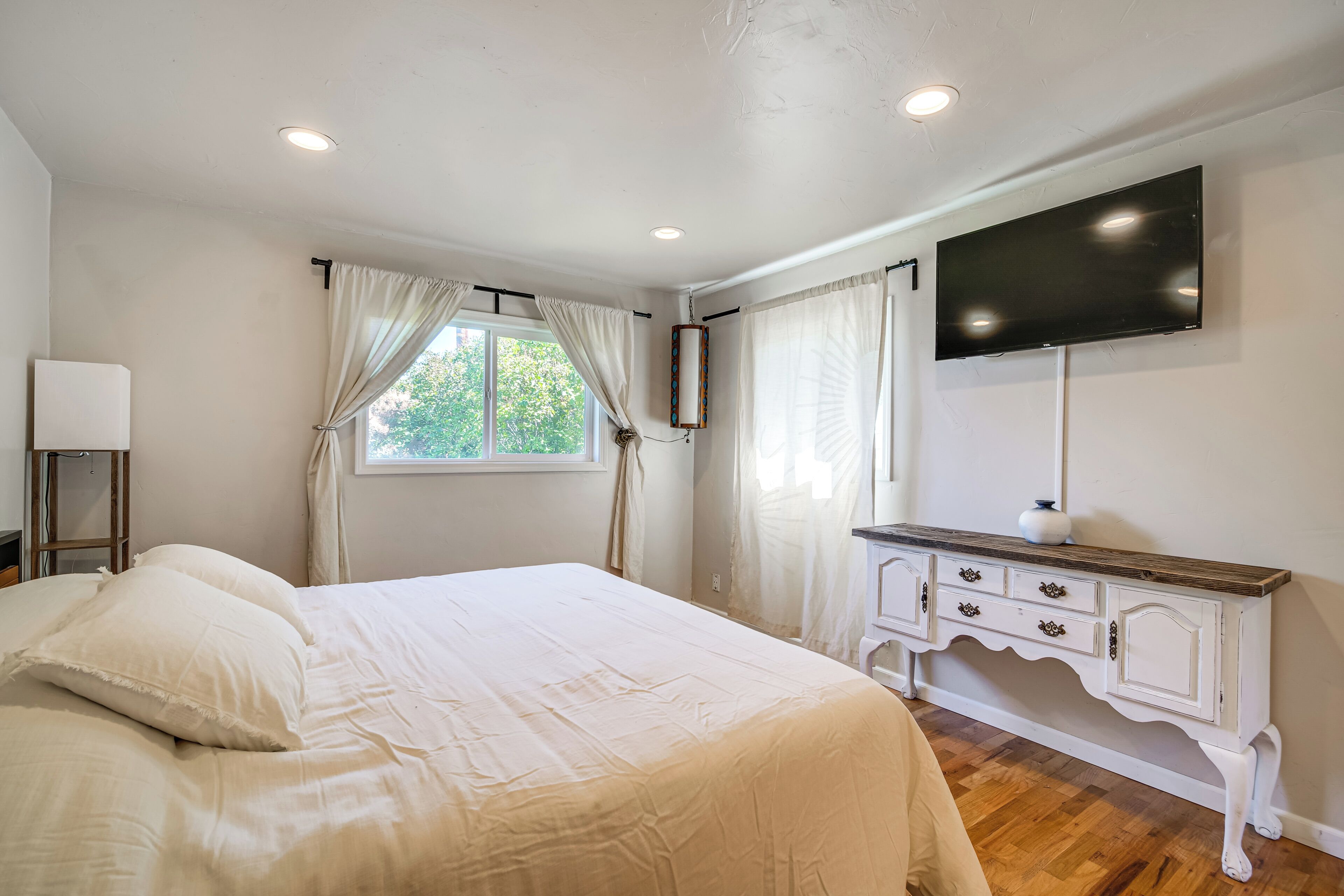 A bedroom with a bed, a dresser, a television, and a window with curtains.