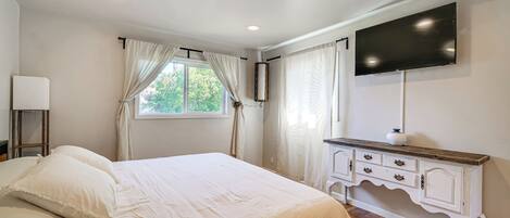 A bedroom with a bed, a dresser, a television, and a window with curtains.