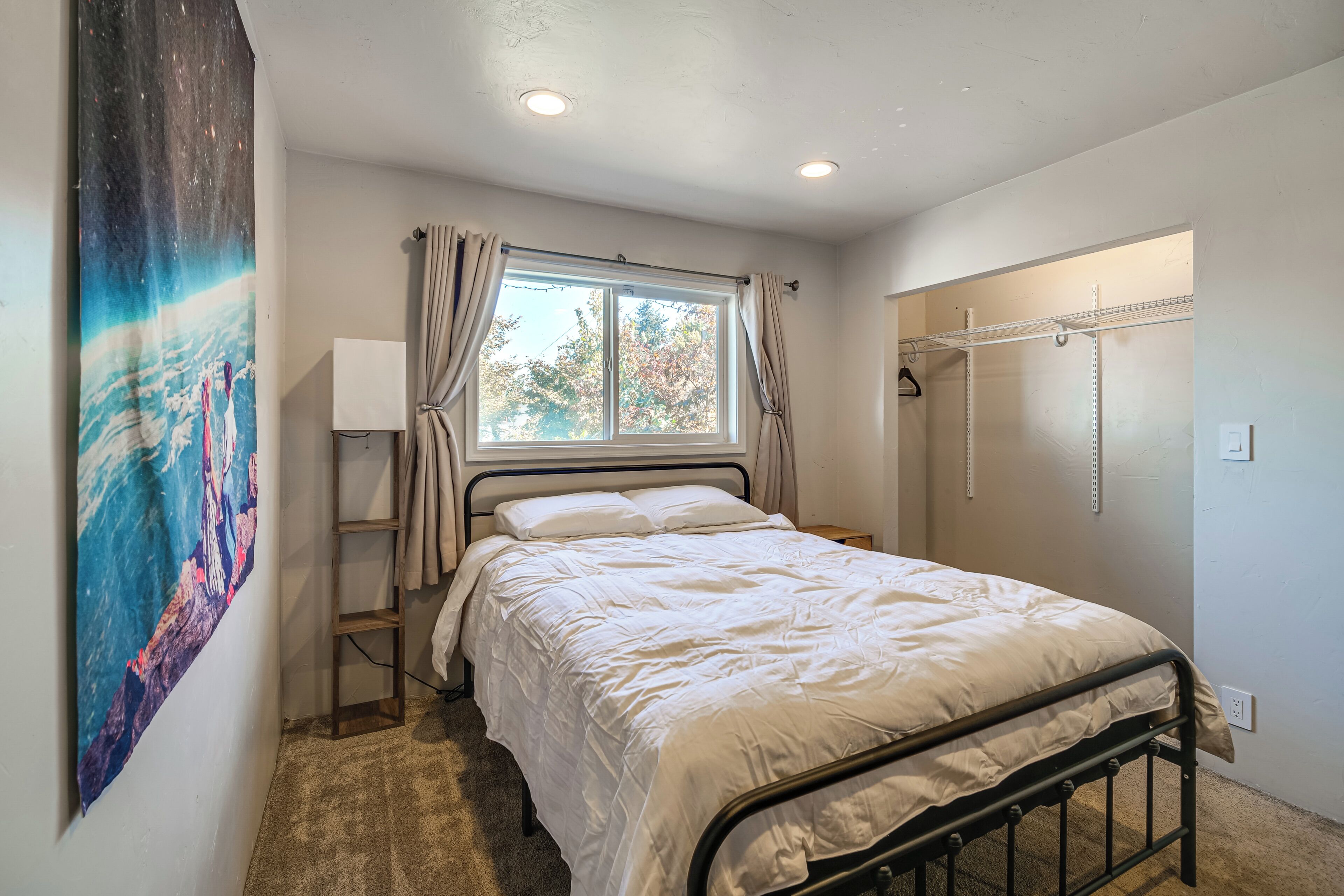 A bedroom with a bed, a window with curtains, a wall-mounted shelf, and a painting.