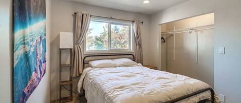 A bedroom with a bed, a window with curtains, a wall-mounted shelf, and a painting.