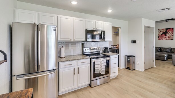 A modern kitchen with stainless steel appliances, white cabinetry, and a wooden dining table. - Fenced-in Yard: Family Home 4 Mi to Dtwn Killeen! (Killeen)