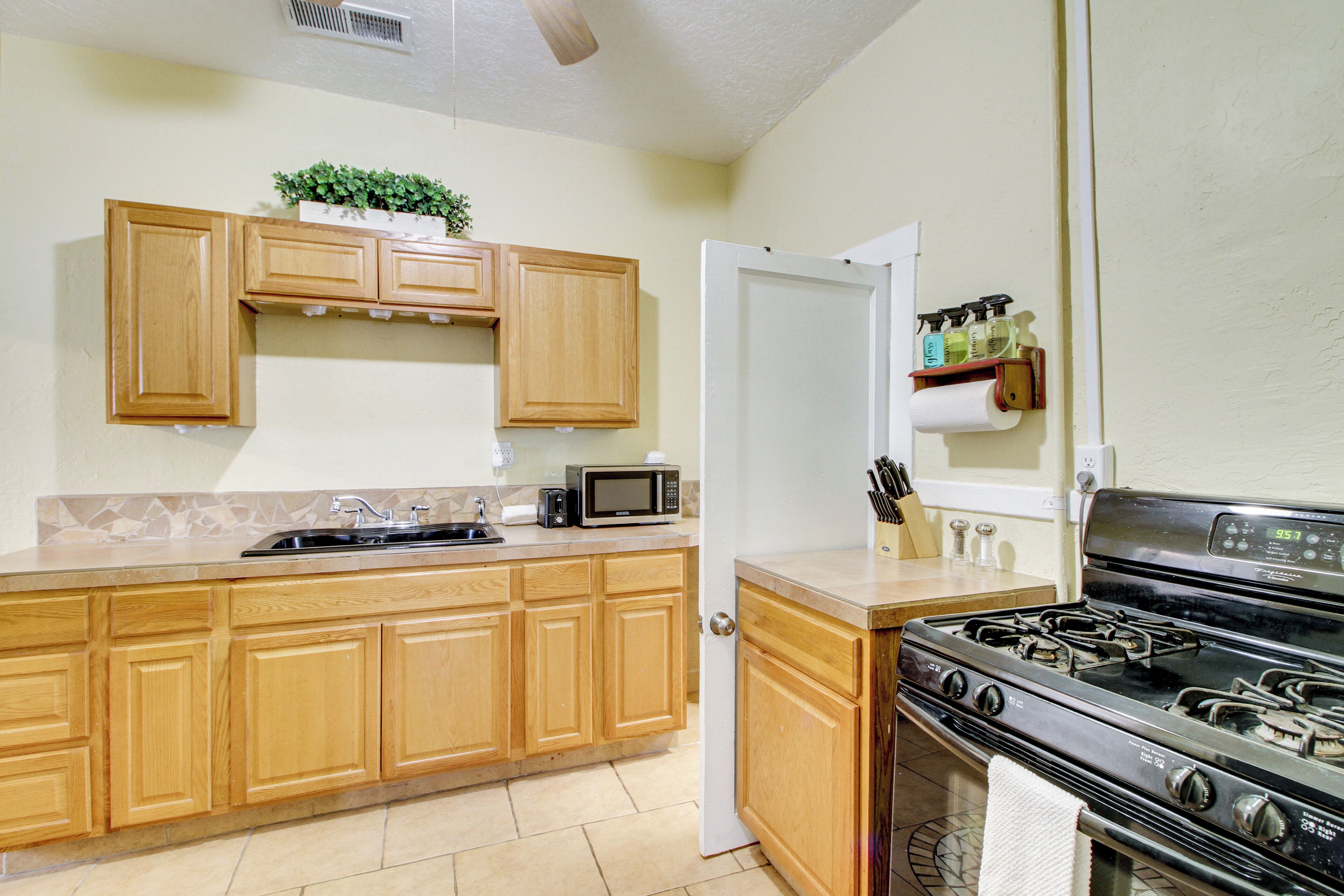 A kitchen with wooden cabinets, a microwave, a stove, and a small shelf with bottles.