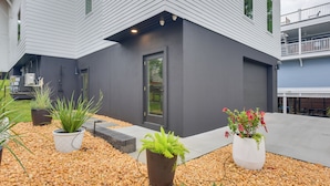 A modern building with a grey exterior, a balcony with railings, and potted plants in the foreground. - Walk to Gulf: Charming Santa Rosa Beach Duplex! (Santa Rosa Beach)