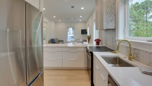 A modern kitchen with a stainless steel refrigerator, white cabinetry, a built-in dishwasher, and a window with a view of trees. - Walk to Gulf: Charming Santa Rosa Beach Duplex! (Santa Rosa Beach)