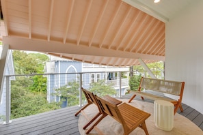 A wooden deck with a table and chairs, a bench, and a white cylindrical object, overlooking a blue house with a white porch. - Stroll to Shore, Modern Santa Rosa Beach Duplex! (Santa Rosa Beach)