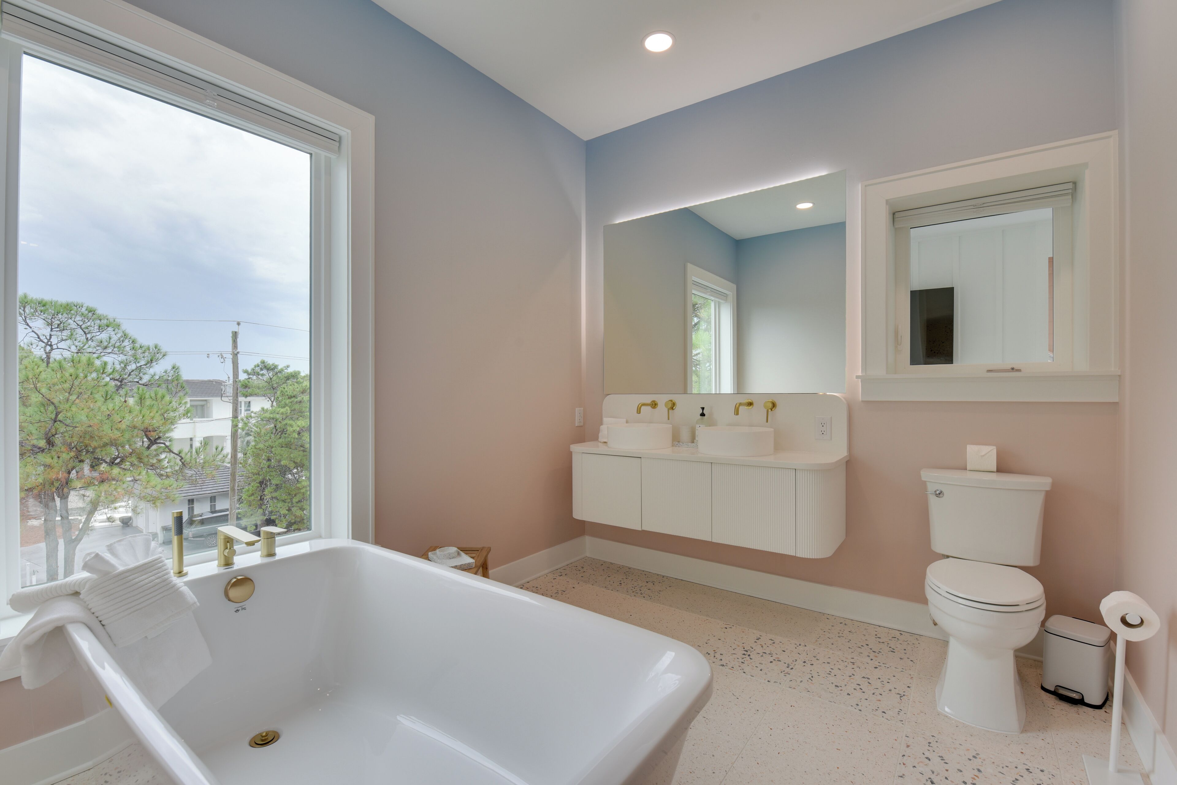 A bathroom with a bathtub, two sinks, a toilet, and a large window.