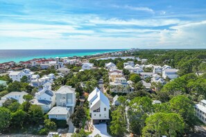 An aerial view of a coastal residential area with houses, dense greenery, and a clear view of the ocean. - Stroll to Shore, Modern Santa Rosa Beach Duplex! (Santa Rosa Beach)